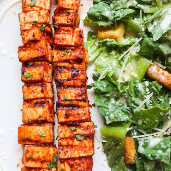 white plate with greek tofu skewers and a side salad 