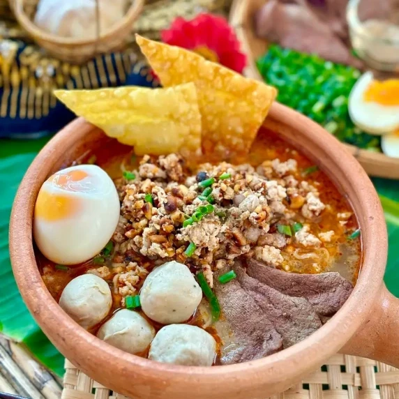 Thai tom yum noodle soup served in a traditional bowl with toppings like egg and pork balls.