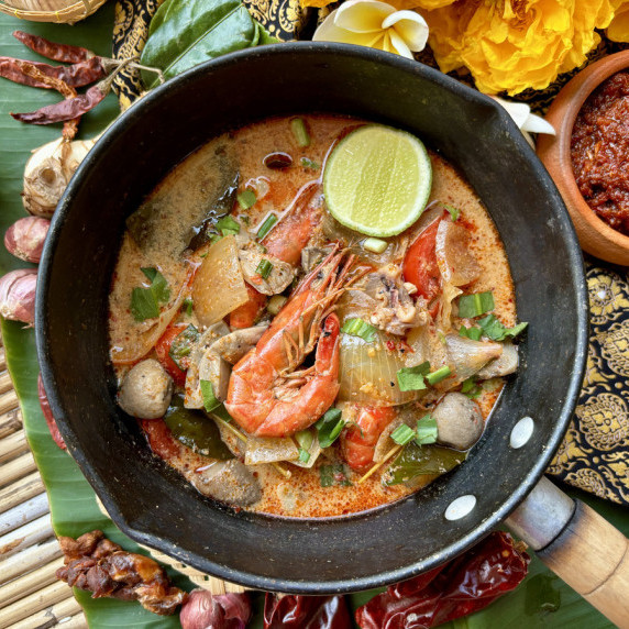Tom yum seafood served in a pan, garnished with fresh herbs and spices.