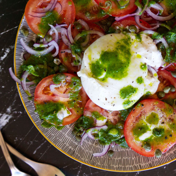A colorful plate of tomato and burrata salad with a reen basil dressing. 