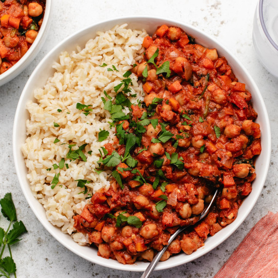 Tomato chickpea stew in a white bowl with brown rice and chopped cilantro.