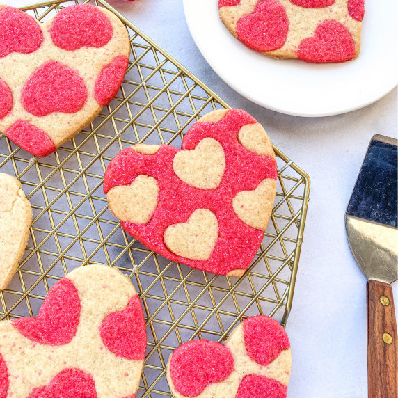 Pink and white heart-shaped Honey Sugar Cookies on a cooling rack.