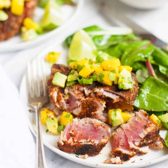 Cut blackened tuna steak topped with mango avocado salsa on a plate with a green salad.