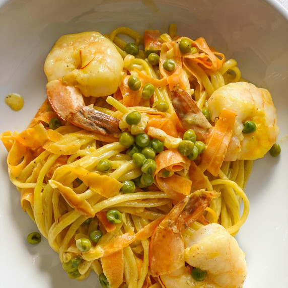 Shrimps, linguine pasta, carrots and peas on a white plate