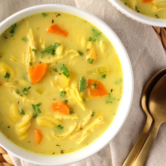 turmeric chicken noodle soup in white bowl garnished with fresh parsley with spoons on the side