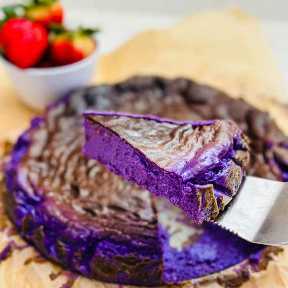 Close-up of a slice of Ube Basque cheesecake, revealing its creamy purple interior with brown crust.