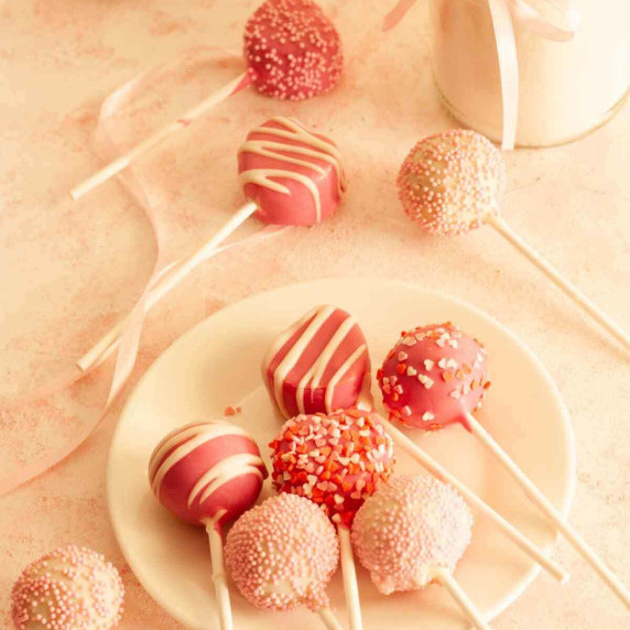 Valentine cake pops on a white plate on a pink and white surface.