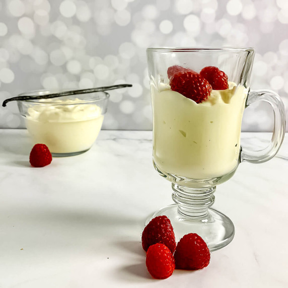 Vanilla pudding in a glass mug with raspberries in front of another glass bowl of pudding with a van