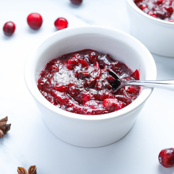 Photo of a bowl of cranberry sauce on a white background with cranberries and star anise scattered.
