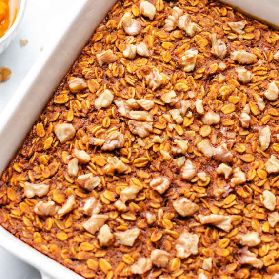 Vegan pumpkin baked oatmeal in a white baking dish with chopped walnuts on top.