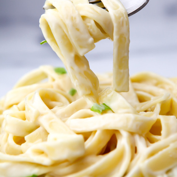 A close up of vegan alfredo sauce on linguini noodles being lifted up with a fork.
