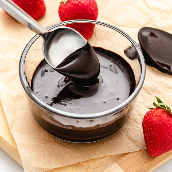 Vegan chocolate sauce in a glass bowl with a spoon dipped in.