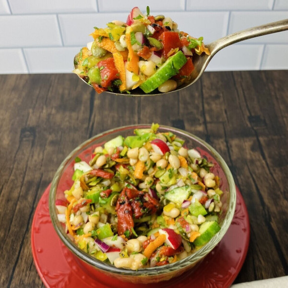 A spoon full of chopped vegan salad hovering above a bowl of the same salad.