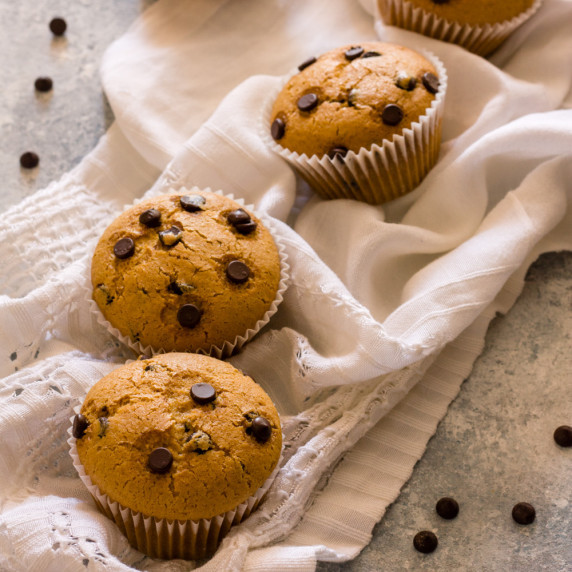 vegan chocolate chip muffins on a white kitchen towel on blue and white counter with chocolate chips