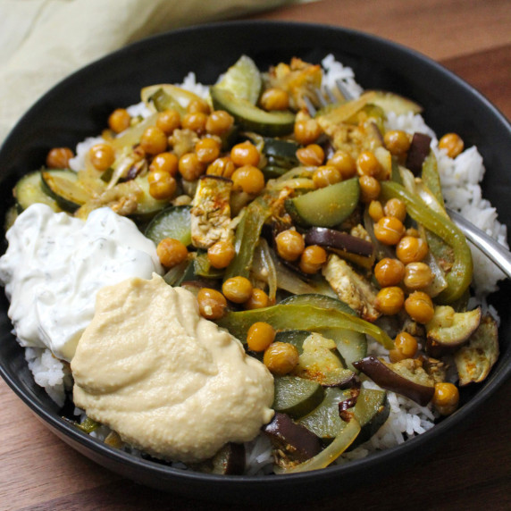 A bowl of Mediterranean roasted veggies and chickpeas with tzatziki, hummus, and basmati rice