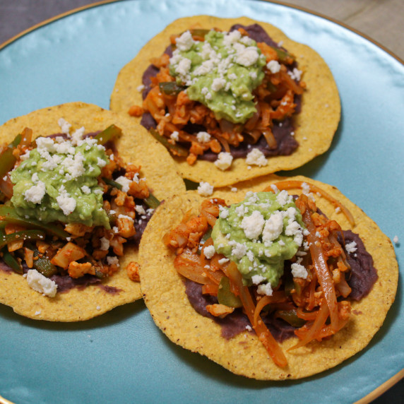 Three tostadas topped with black beans, spicy vegetables, guacamole, and queso fresco