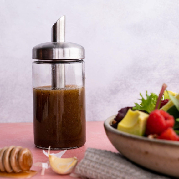 A glass cruet filled with balsamic vinaigrette stands beside a colorful fresh salad in a bowl.