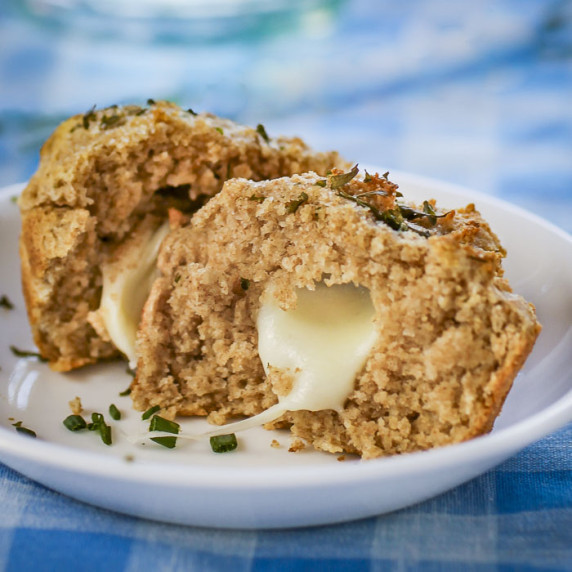 Side shot of a biscuit split in half with mozzarella inside garnished with fresh herbs.