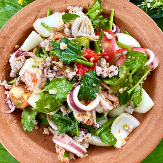 Yum talay (spicy Thai seafood salad) in a clay dish, made with vegetables, squid, shrimp, and more.