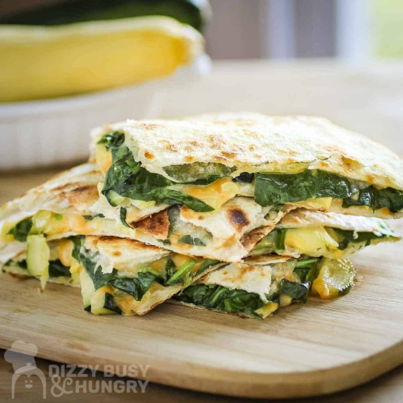 Overhead shot of three halves of spinach quesadillas stacked on a wooden cutting board.